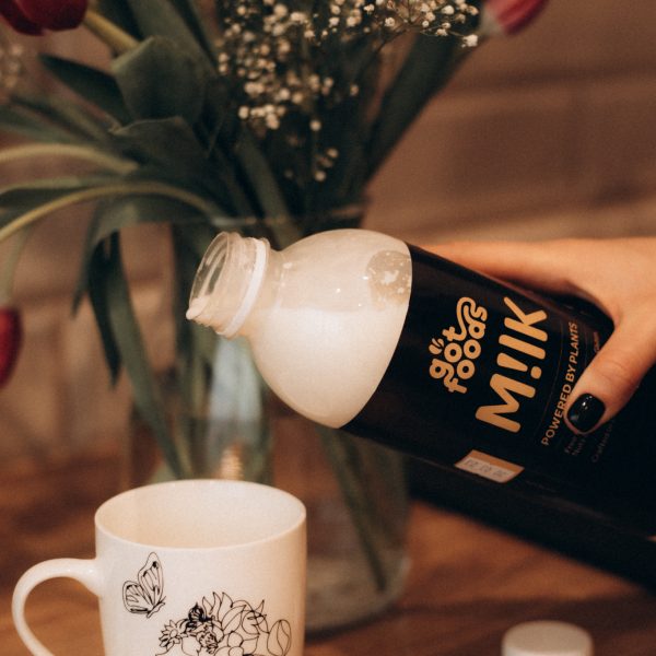 Vegan milk being poured in a cup with flowers in the background