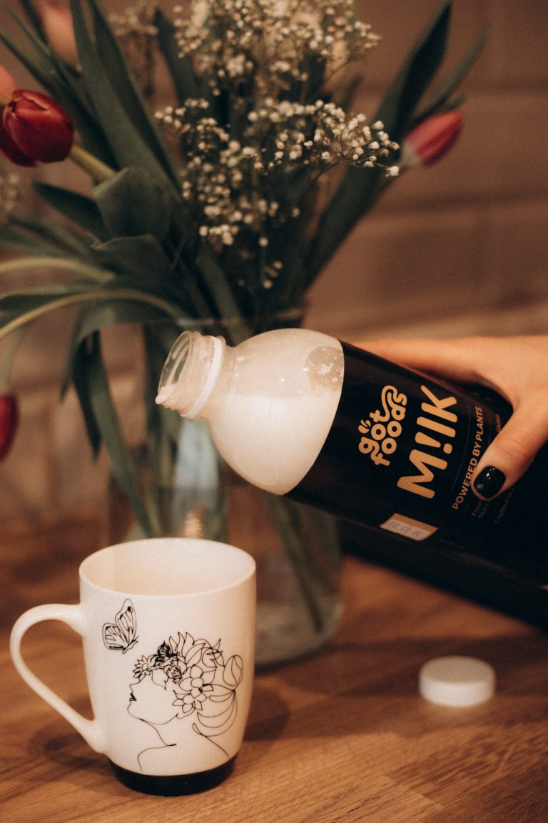 Vegan milk being poured in a cup with flowers in the background